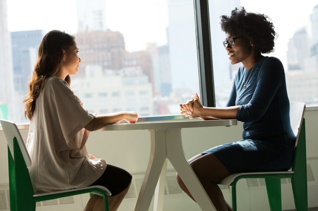 Dos mujeres conversando en una reunión profesional. Imagen ilustrativa sobre emprendimiento femenino.